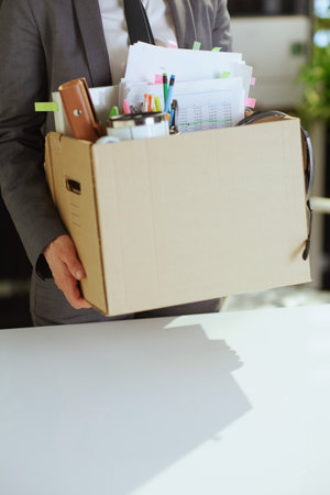 New job. Closeup on modern woman worker in modern green office in gray business suit with personal belongings in cardboard box.の写真素材