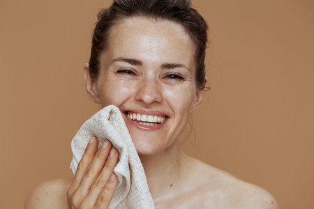 smiling middle aged woman with towel washing face against beige background.の写真素材