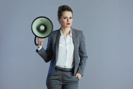 trendy 40 years old business woman in gray suit with megaphone against gray background.の写真素材