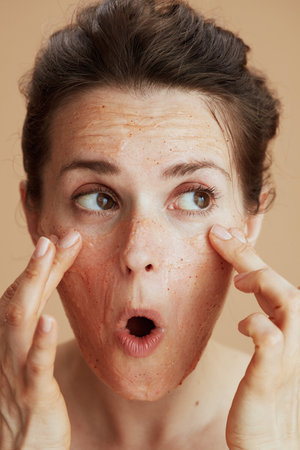young 40 years old woman with face scrub isolated on beige.の写真素材