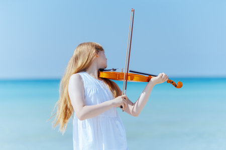 modern teenage girl in white dress on the ocean coast with violin enjoying playing.の写真素材