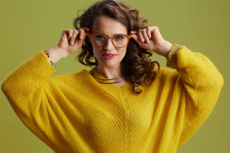 Portrait of trendy female against green background in yellow sweater and glasses.