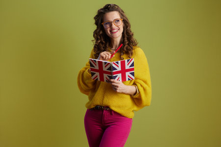 happy fit woman against green background in yellow sweater and glasses with a notepad in colors of the British flag.の写真素材
