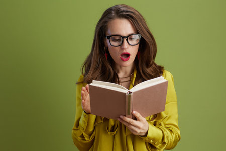 surprised healthy woman on green background in green blouse and glasses with book.