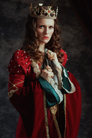 furious medieval queen in red dress with handkerchief and crown on dark gray background.の写真素材