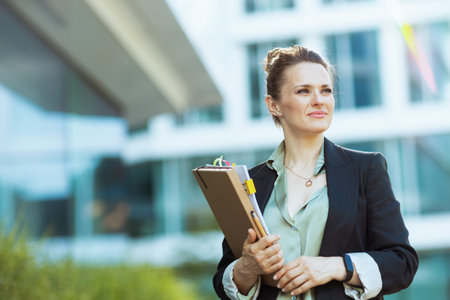 pensive modern 40 years old business woman near office building with documents and folder.の写真素材