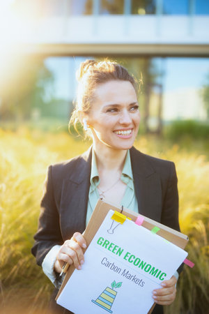 smiling modern female worker near business center in black jacket with documents and folder.の写真素材