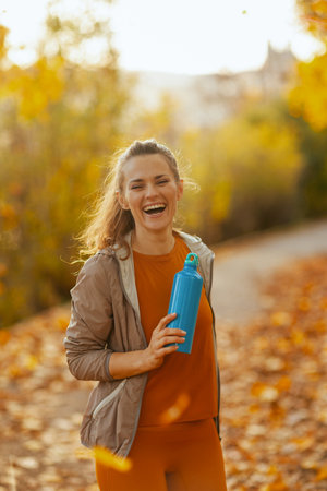 Hello autumn. smiling fit 40 years old woman in fitness clothes in the park with bottle of water.の写真素材