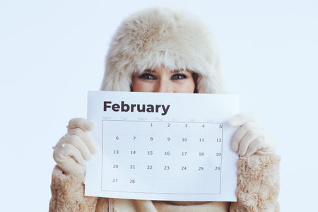 happy stylish woman in winter coat and fur hat isolated on white in white gloves with february calendar.の写真素材