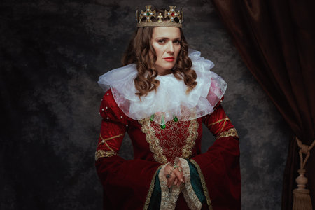 medieval queen in red dress with white collar and crown on dark gray background.の写真素材