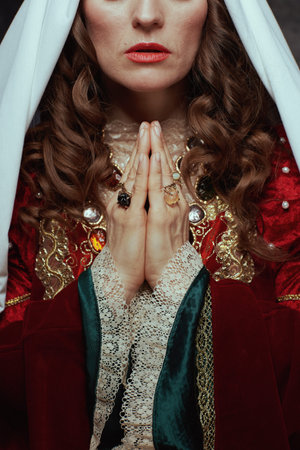 Closeup on medieval woman in red dress with veil praying.