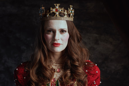 medieval queen in red dress with white makeup and crown on dark gray background.の写真素材