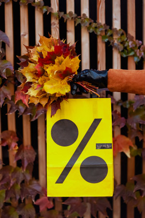 Hello September. Closeup on trendy middle aged woman in brown trench coat with shopping bag and autumn yellow leaves in the city.の写真素材