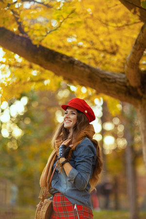 Hello autumn. smiling elegant woman in jeans shirt and red hat with scarf and gloves in the city park.の写真素材