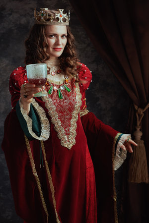 medieval queen in red dress with goblet and crown on dark gray background.の写真素材