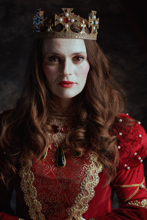 medieval queen in red dress with white makeup and crown on dark gray background.の写真素材