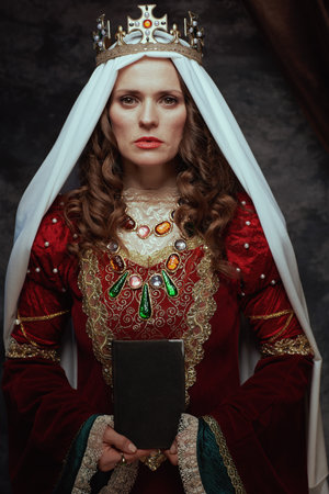 medieval queen in red dress with book, veil and crown on dark gray background.の写真素材