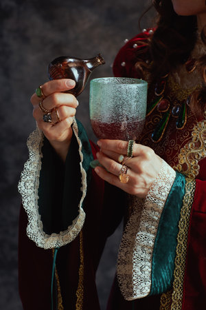 Closeup on medieval queen in red dress pouring liquid into the goblet on dark gray background.の写真素材