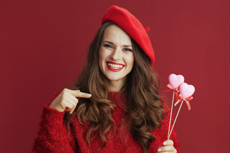 Happy Valentine. smiling stylish 40 years old woman in red sweater and beret with hearts on stick.の写真素材