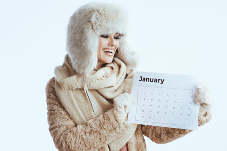 smiling stylish woman in winter coat and fur hat against white background in white gloves with january calendar.の写真素材