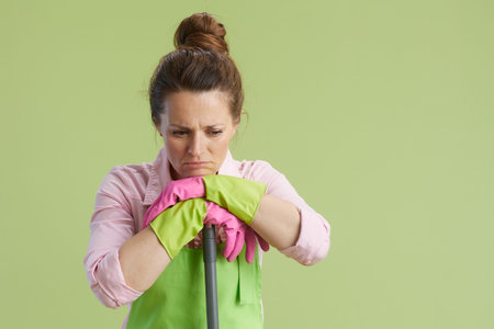 Spring cleaning. sad modern woman in green apron and rubber gloves isolated on green with mop.