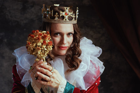 medieval queen in red dress with dried flower, white collar and crown on dark gray background.の写真素材