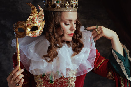 medieval queen in red dress with venetian mask, white collar and crown on dark gray background.