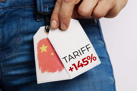 A hand lifts a jeans price tag showing a Chinese flag and a 145% tariff, emphasizing the personal...