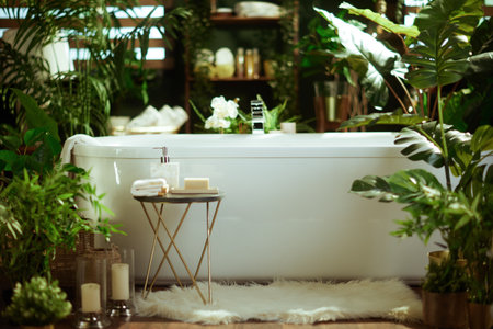 A modern white bathtub in a lush, plant-filled bathroom, with a side table, soft rug, & candles. This tranquil scene portrays an inviting, spa-like atmosphere for relaxation & luxury.の写真素材