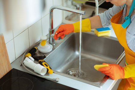 Gloved hand turns on the kitchen faucet to check water flow and see if the recent clogged-sink repair has solved the drainage problem.の写真素材