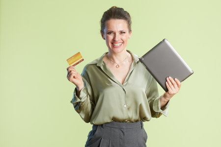 A smiling woman with a tablet and credit card suggests easy e-commerce and financial transactions, against a soft light green background.の写真素材