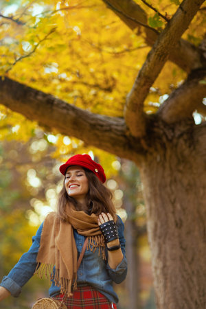 Hello autumn. smiling elegant woman in jeans shirt and red hat with scarf and gloves in the city...