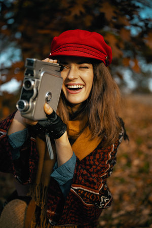Hello autumn. smiling stylish woman in red hat with retro video camera, scarf and gloves in the city...