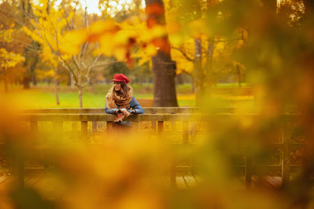 pensive stylish female in jeans shirt and red hat with autumn leaf and scarf in the city park.