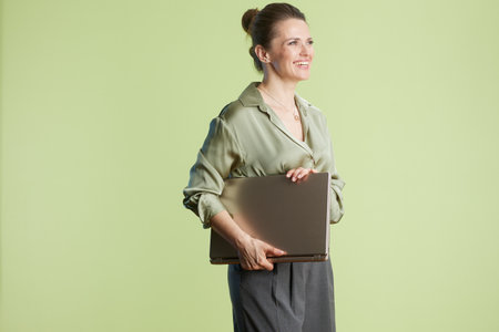 A smiling woman holds a laptop against a light green background, creating a bright and professional atmosphere ideal for business and career themes.の写真素材