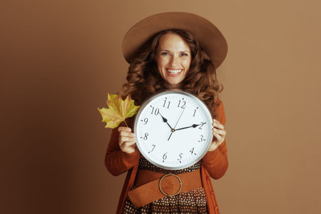 A happy woman in autumn attire, featuring a wide-brimmed hat and orange cardigan, smiles broadly...