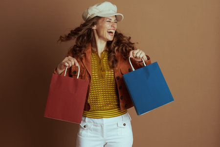 A laughing woman with long curly hair, dressed in a brown jacket and cap, holds red and blue...