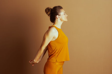 A woman in a mustard yellow top and leggings stretches peacefully in side profile, eyes closed and...