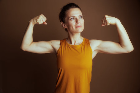 A determined woman in a bright yellow tank top flexes her bicep, looking upwards with focus. This...