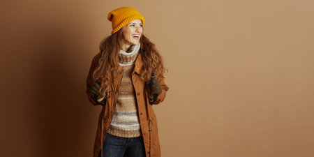 A cheerful woman with long brown hair, sporting a yellow knit hat, brown jacket, and striped...
