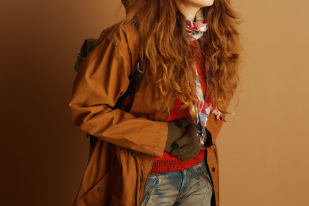 A woman in a stylish layered autumn outfit, including an orange sweater, brown jacket, and plaid...