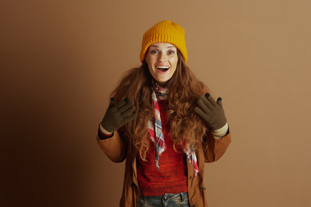 An excited woman in warm autumn-winter clothing, including a beanie and knit sweater, gestures expressively while looking directly at the camera with wide eyes and an open mouth.の写真素材