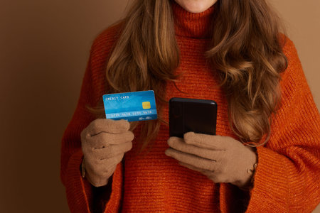 A close-up shot of hands in cozy fall gloves, holding a smartphone and credit card, illustrating the...