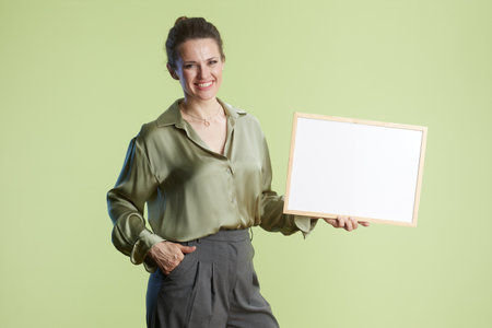 A smiling woman holds a blank white sign, hand in pocket, against a light green backdrop. Friendly and professional presentation.の写真素材