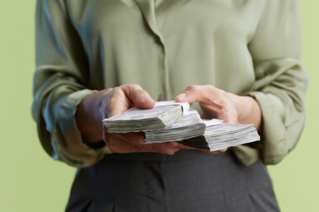 A person holds a stack of wrapped hundred-dollar bills, representing wealth, financial transactions,...