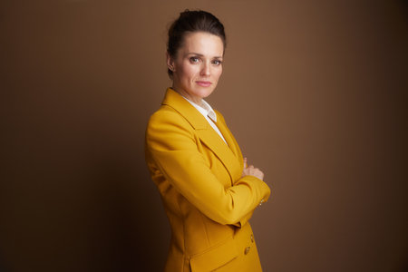 A professional woman in her 40s, wearing a yellow blazer, confidently crosses her arms while looking directly at the camera, conveying a serious and empowered demeanor.の写真素材