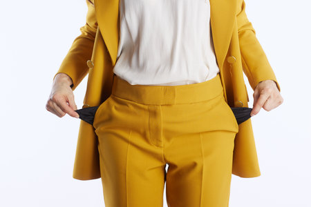A close-up of a person in a mustard yellow business suit pulling out empty pockets, powerfully symbolizing financial difficulty, debt, or a lack of funds in a minimalist studio.の写真素材