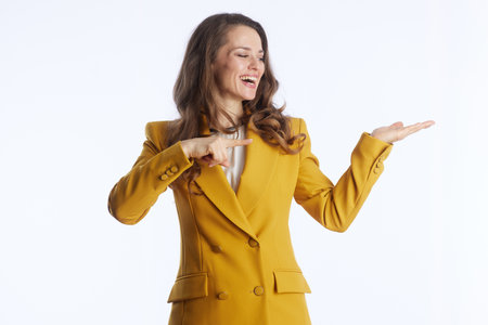 A smiling woman in yellow blazer and white shirt confidently points right, left palm open in presenting gesture. Against bright white background, she conveys clear direction and information sharingの写真素材