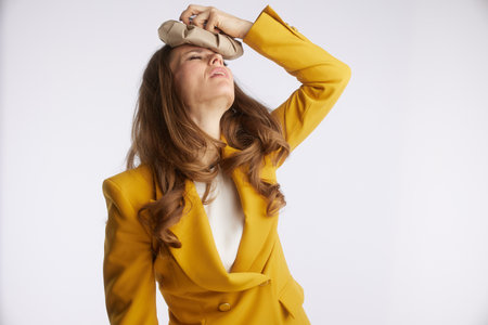 A businesswoman with a pained expression holds an ice pack to her forehead, reflecting moments of discomfort, stress, or the need for self-care in a demanding professional life.の写真素材