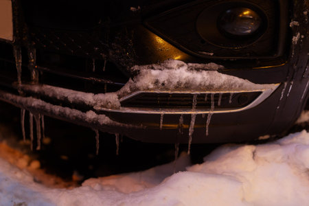 Close-up of a dark car front grille and bumper heavily coated in frost and hanging icicles, illustrating the effects of extreme winter temperatures.の写真素材